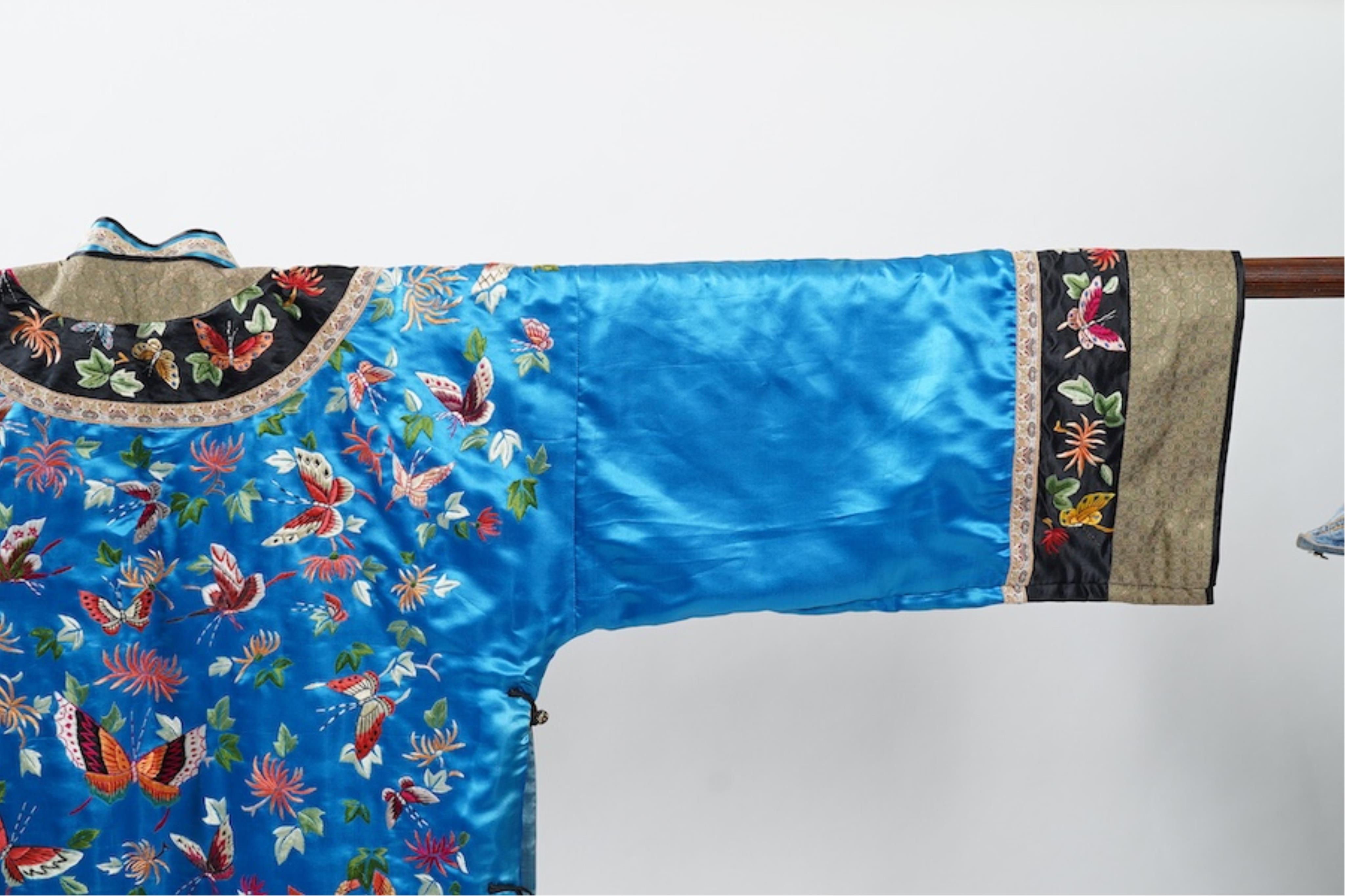 A mid 20th century Chinese turquoise silk jacket, with all over polychrome butterfly embroidery, similar embroidered sleeve bands, front and bottom edges on black silk, all bordered with gold brocade. The jacket blue sil